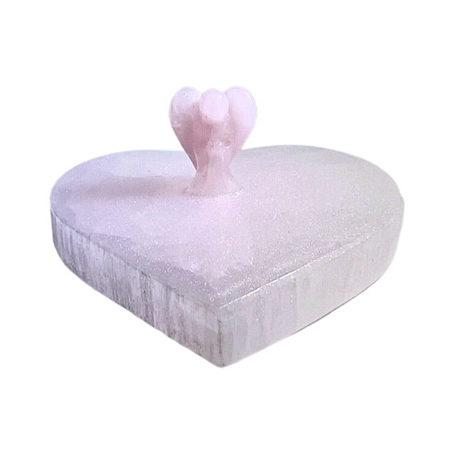 A stunning selenite heart charging plate featuring a beautiful pink shimmery patina and a rose quartz angel centerpiece. Top angled view