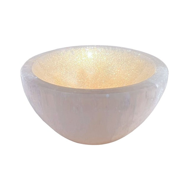A petite selenite crystal bowl, tilted forward and hand adorned with a golden finish.