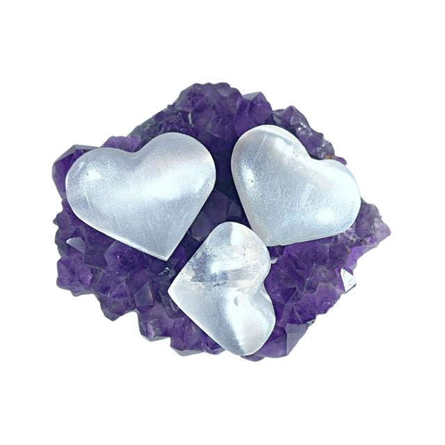Three glam selenite puffy crystal hearts, hand-painted with a custom opalescent patina, sitting atop a deep purple amethyst cluster from Uruguay.