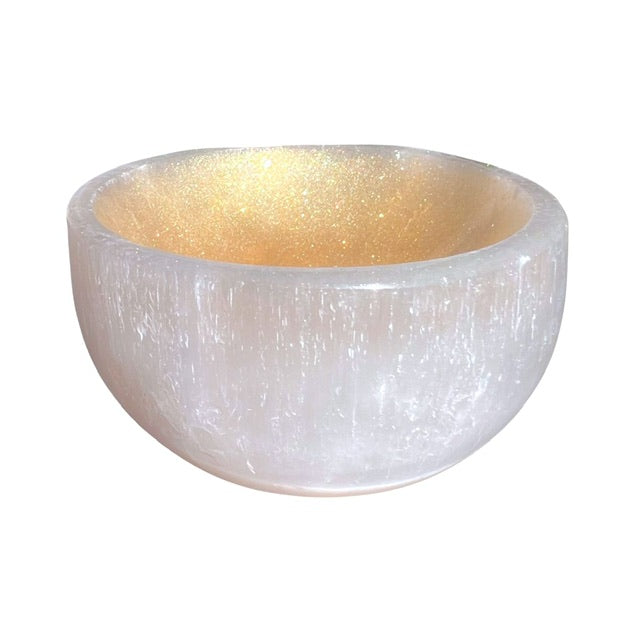 A petite selenite crystal bowl, tilted forward and hand adorned with a golden finish.