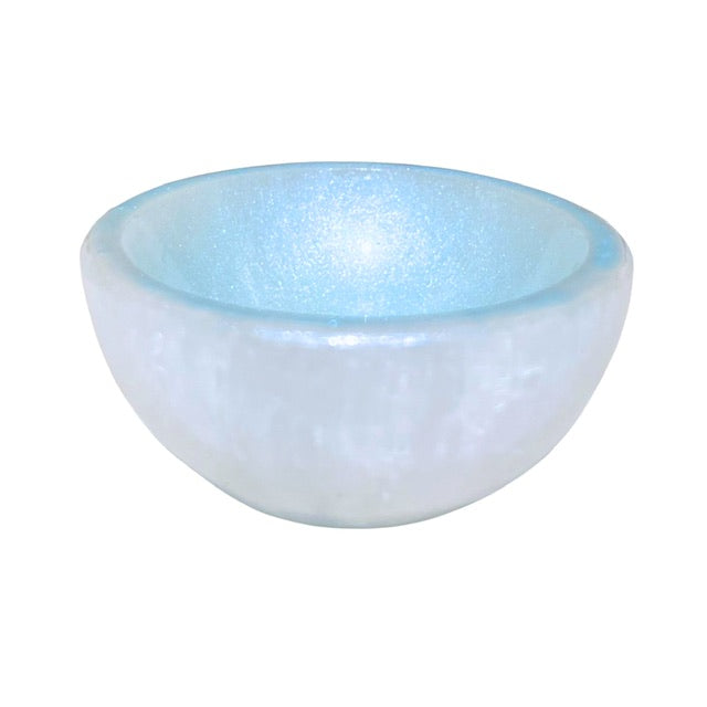 A petite selenite crystal bowl, tilted forward and hand adorned with a sky blue finish.