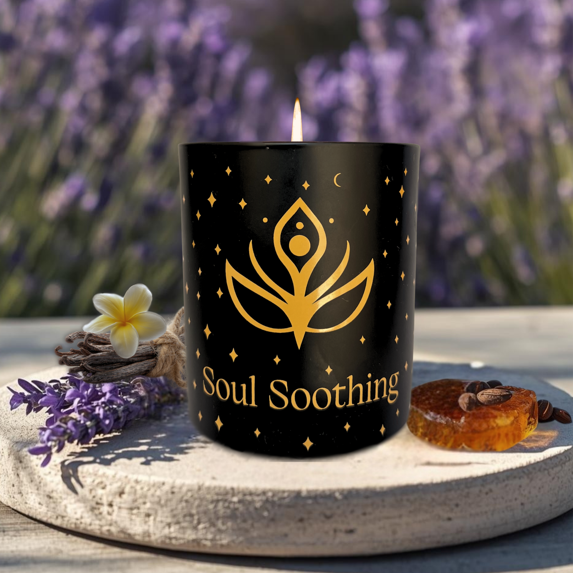 Intention Illuminating black 'Soul Soothing' candle with a gold icon, surrounded by lavender, vanilla flowers and amber on a stone surface.